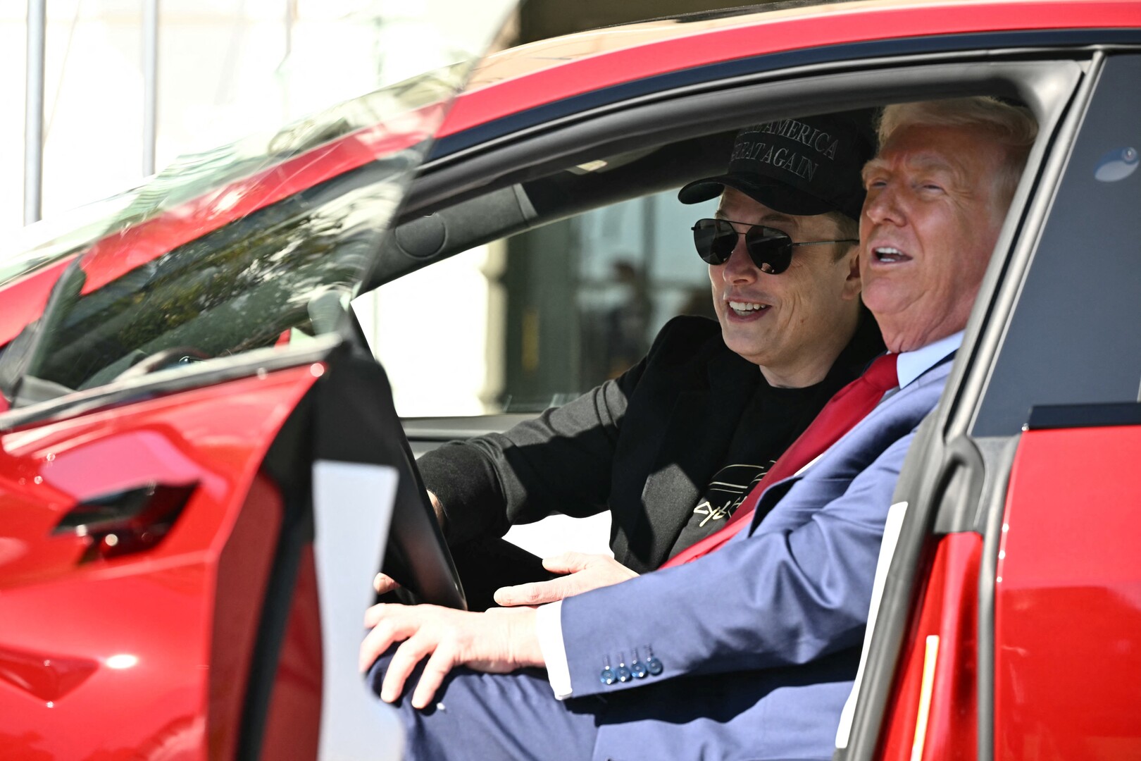 Donald Trump and Elon Musk in a red Tesla.